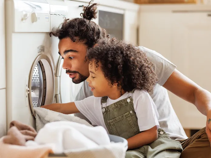 Father helping child fill washing machine